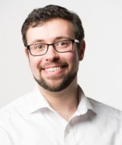 Matt McCarty smiles at the camera. He wears a white button up shirt and glasses.